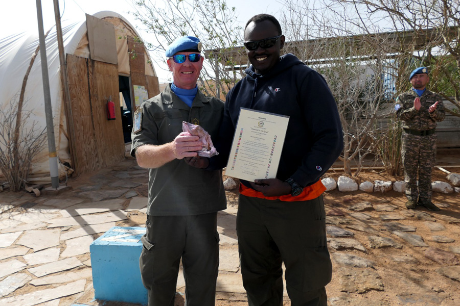 A man receiving an award from a male uniformed soldier wearing a blue cap.