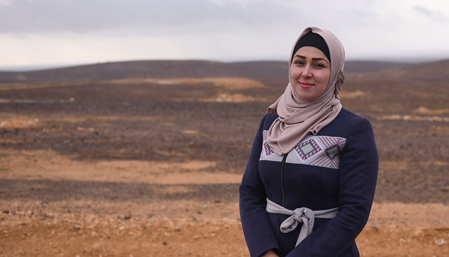 Portrait of a woman standing in a vast, arid landscape under cloudy skies.