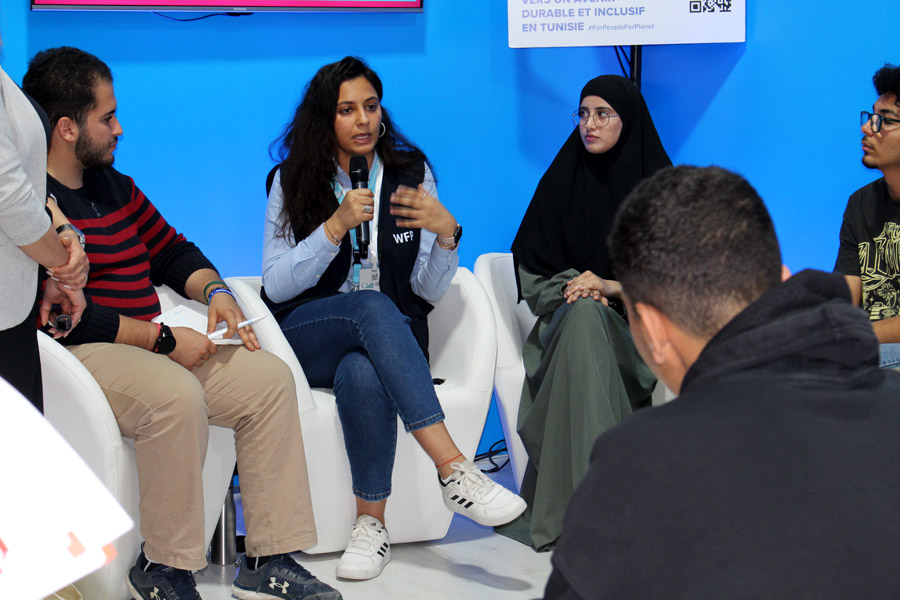 A woman wearing a WFP-branded vest leading a discussion with attendees at an event.